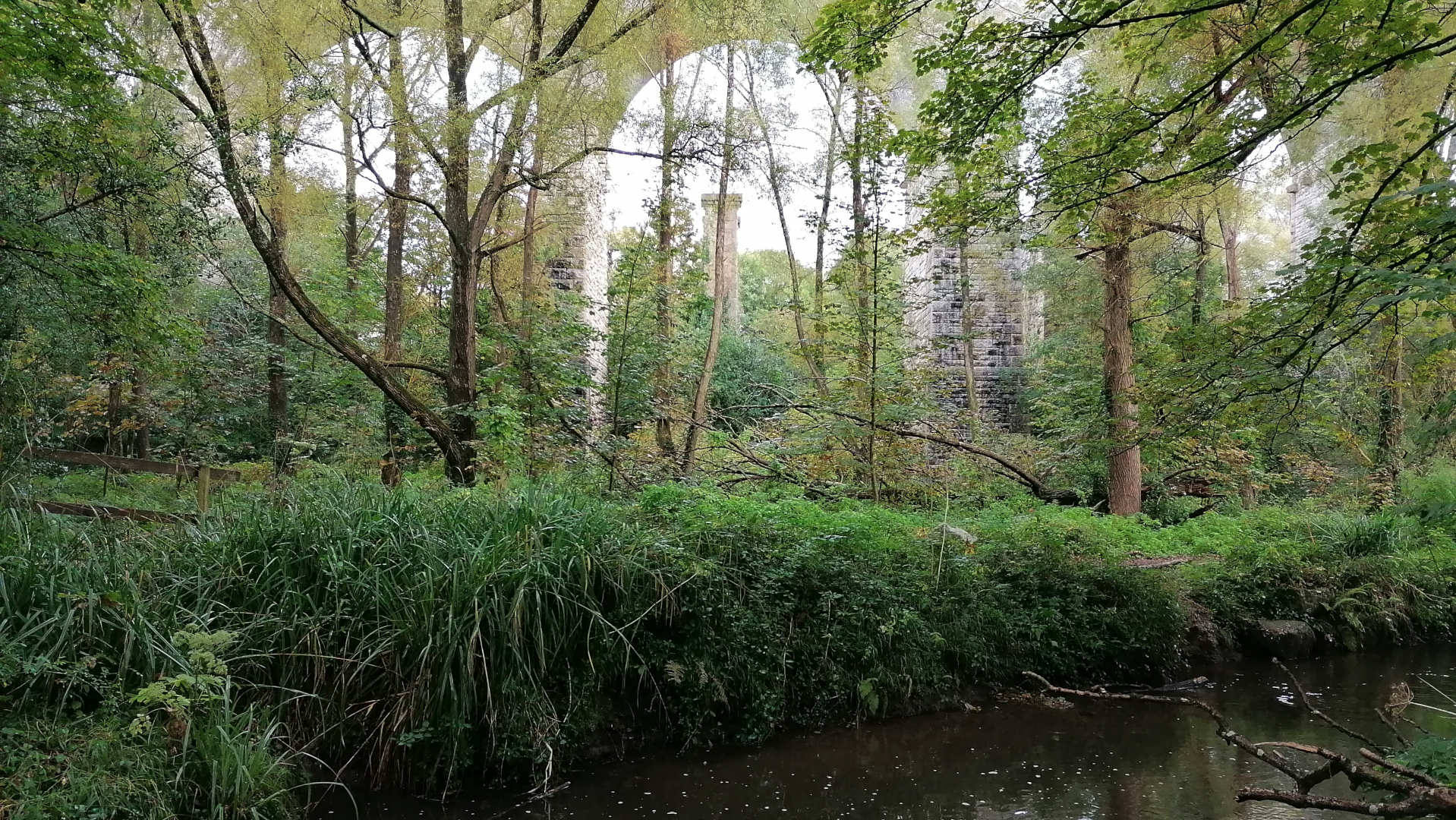 A close-up view of Leonie's feet clad in brown leather hiking boots, standing on a snowy ground. The boots are laced up and appear sturdy, suitable for winter conditions. A portion of a chunky, multicoloured knit scarf is visible wrapped around the ankles. The snow is lightly covering the ground, with some patches appearing denser than others. The overall impression is one of cold weather and outdoor activity.