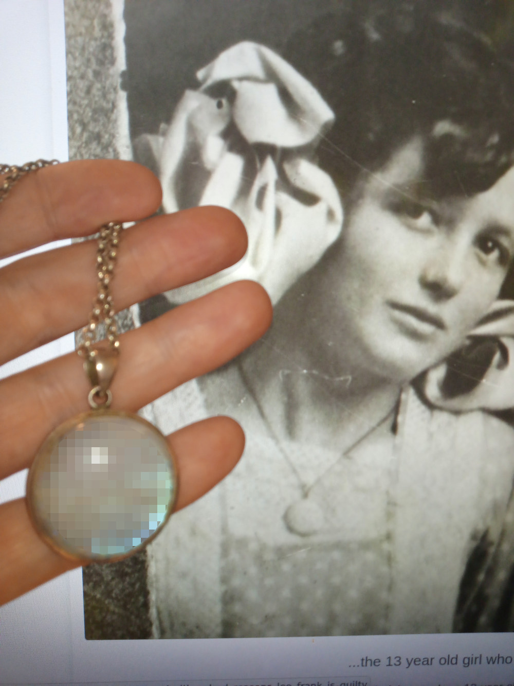 Leonie's hand holding a silver necklace with a round, iridescent pendant. Behind the hand and necklace is a black and white photograph of a young woman, possibly a teenager, in what appears to be period clothing. The photo's quality is somewhat low, and part of the image is obscured by the hand. A caption at the bottom of the photo partially visible, suggesting a story or context related to the girl in the photo. The overall impression is one of juxtaposition, of a modern hand holding an object possibly connected to the historical image of the young woman.