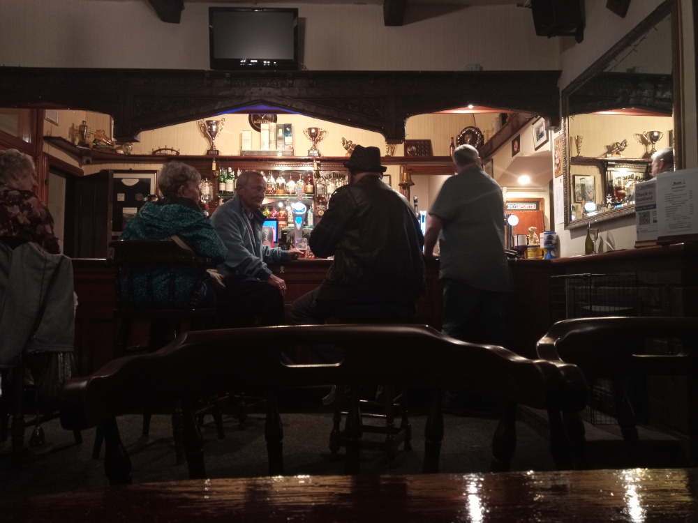 Dimly lit pub interior, focusing on a group of patrons seated at the bar.