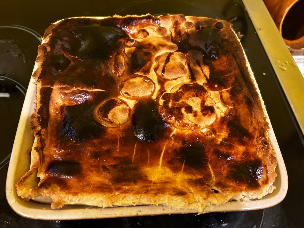 Rectangular baking dish containing a baked pie with a deeply browned, glossy crust. The crust exhibits some uneven browning, suggesting areas of higher heat exposure during baking. The pie appears to be filled, though the filling itself is not visible.