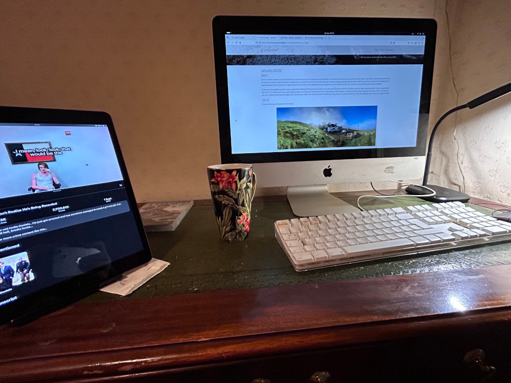 Desk with a computer, tablet, and keyboard. A mug sits between the computer and the tablet. The computer displays a web page with text and a picture of a steam train in a landscape. The tablet shows a video screen capture. The overall scene suggests a workspace, perhaps for writing or content creation, possibly related to trains or travel based on the computer screen's content.