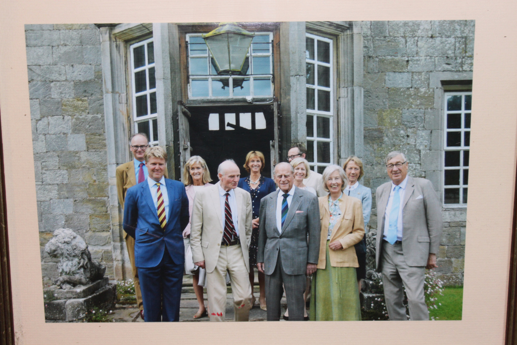Group photograph of ten people, formally dressed, standing in front of a stone building with multiple windows. The group includes both men and women and appears to be a formal occasion. The central figures are an older man and woman who are significantly more prominent than the others in the photo. The architecture suggests a stately home or castle setting. The overall impression is one of formality and possibly a commemorative or celebratory event.