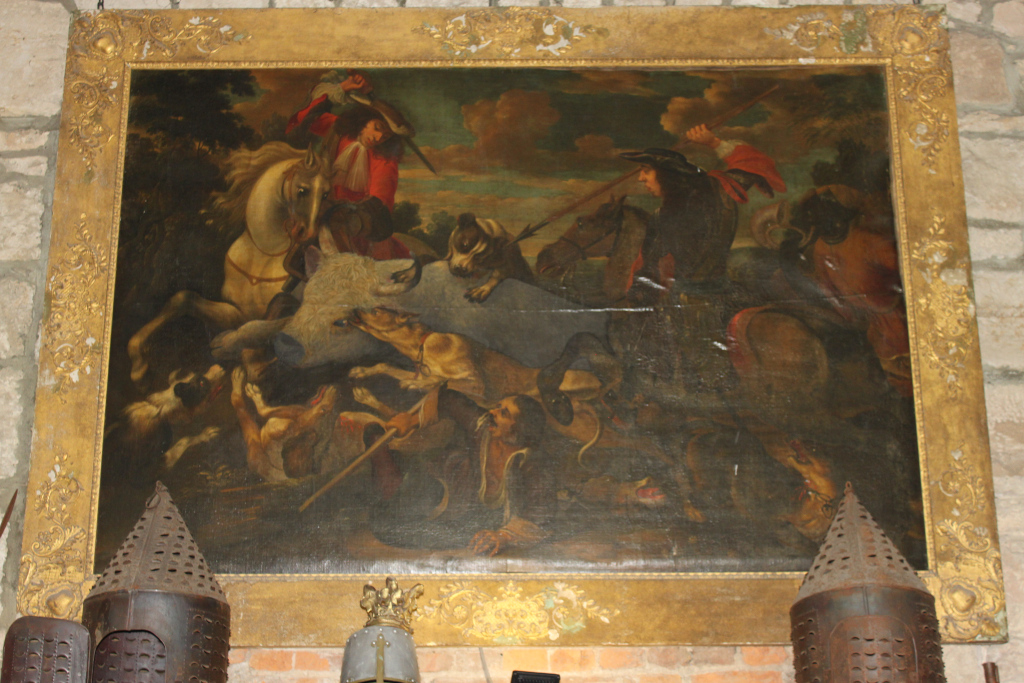 Large oil painting depicting a boar hunt. The scene is dynamic, featuring several mounted hunters attacking a boar with the help of hounds. The painting is richly Coloured and detailed, showcasing the action and excitement of the hunt. The style suggests it's possibly from the Baroque period. The painting is framed in a large, ornate gilt frame.