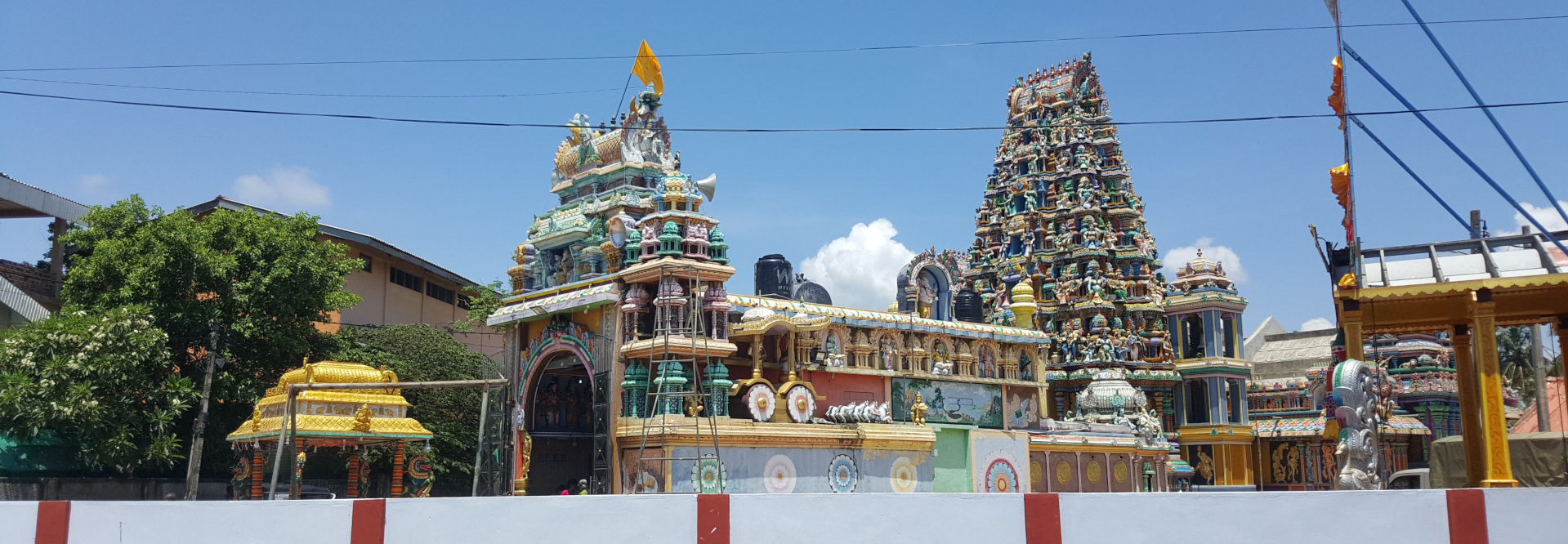 Vibrant and intricately decorated Hindu temple complex, seemingly situated in an urban or suburban area. The main focus is on two gopurams (towering entrance structures).