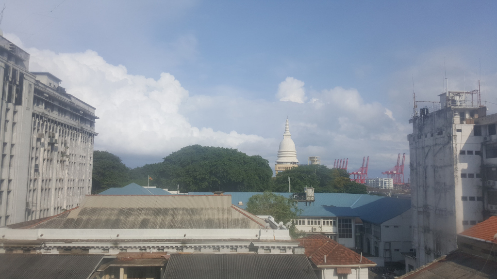 Urban cityscape, viewed from a slightly elevated perspective, likely from a window. No people are visible. 