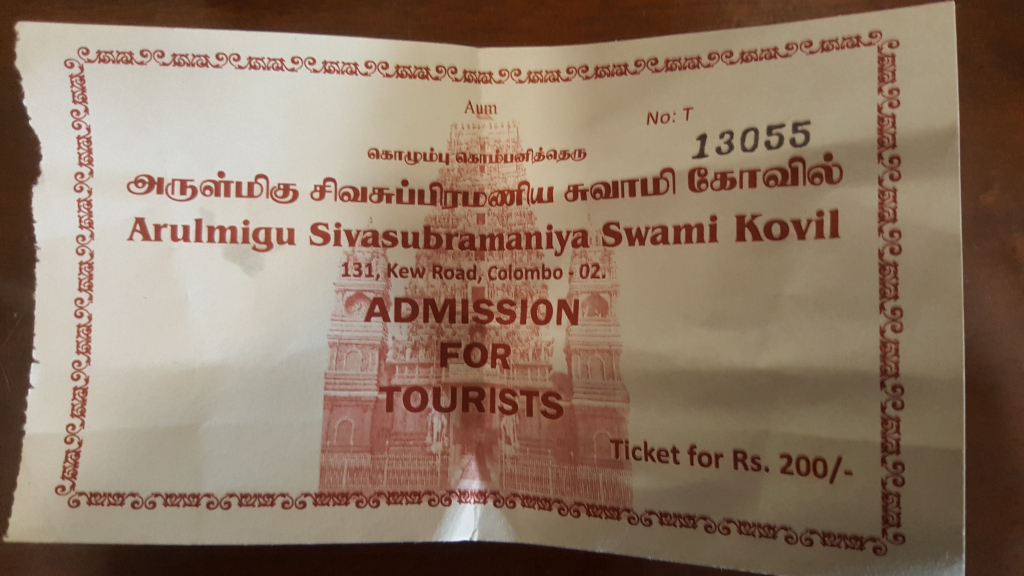 Slightly crumpled, off-white admission ticket to the Arulmigu Sivasubramaniya Swami Kovil temple in Colombo, Sri Lanka. The ticket is rectangular with a decorative border composed of repeating swirling patterns in a dark reddish-brown ink. The text is primarily in Tamil and English, with the temple name prominently displayed. A small image of the temple's gopuram (tower) is centrally positioned below the text, rendered in the same reddish-brown. The ticket number (13055) is clearly visible, as is the price (Rs. 200/-). There are no people visible.